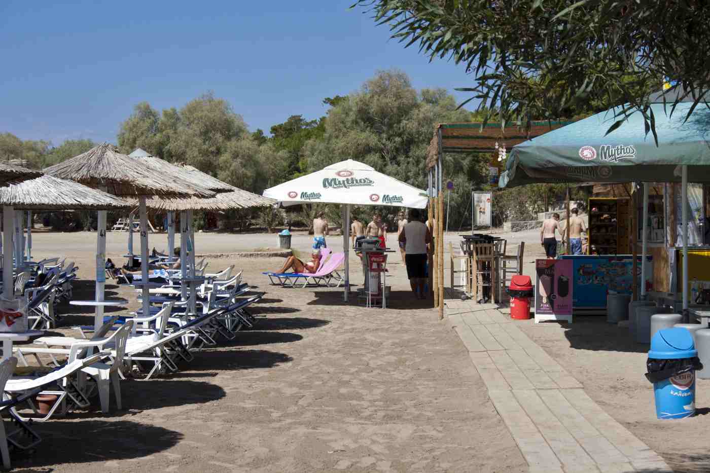 An organised sandy beach with thatched umbrellas and shade trees on Aegina