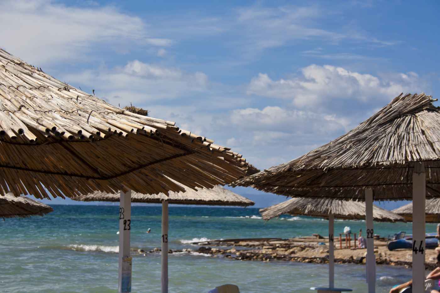 Thatched sun umbrellas above the clear blue sea on a beach in Aegina
