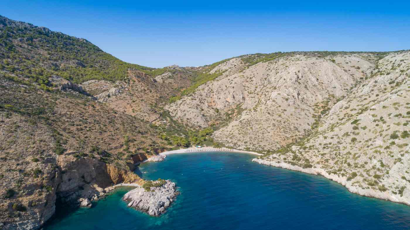 Aerial view of Agios Nikolaos bay on Hydra, its turquoise water and pebble beach ringed by hills