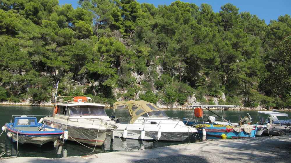 Small boats moored in a pine-fringed cove on Paxos
