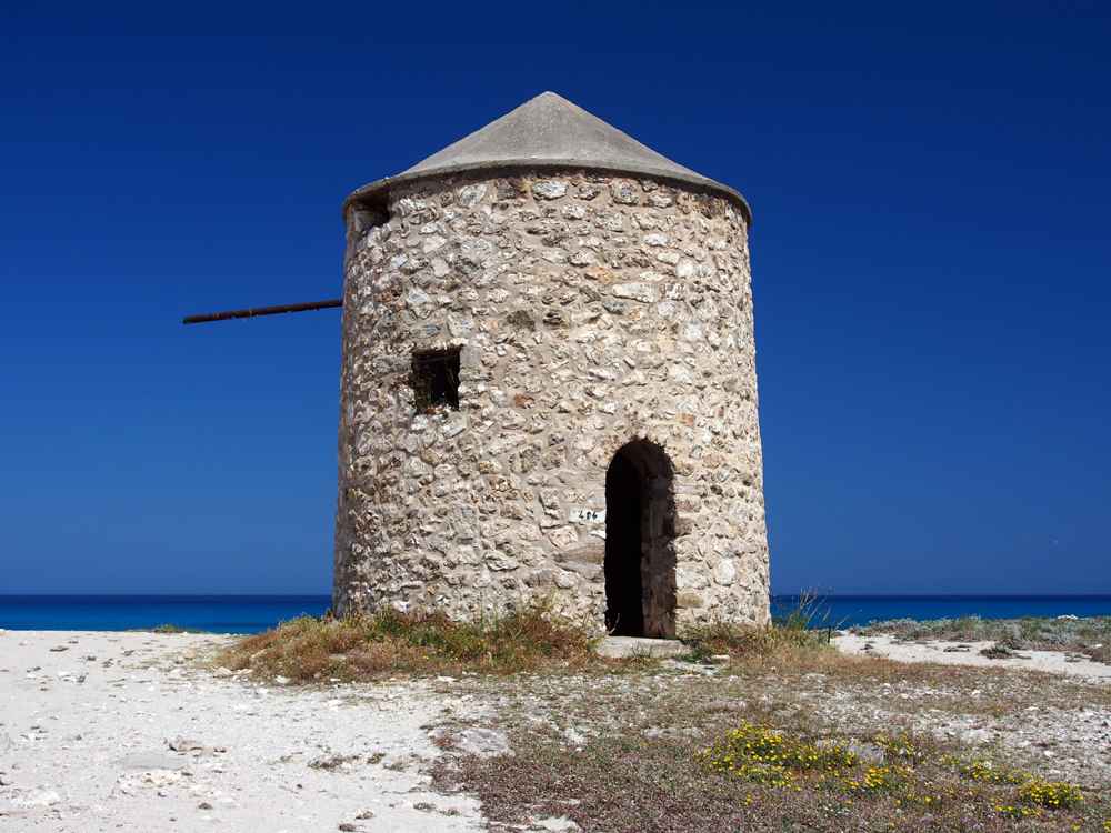 Old stone windmill on Gyra beach with the sea on either side, Lefkada