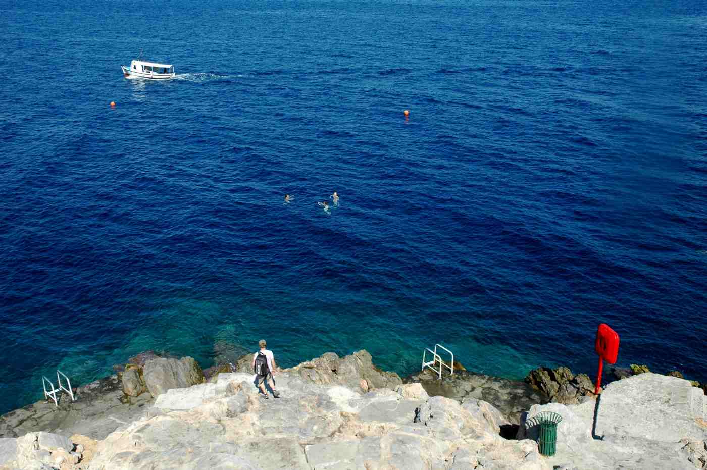 Hydra boat trips: a small boat and swimmers in the clear blue sea off the rocky coast