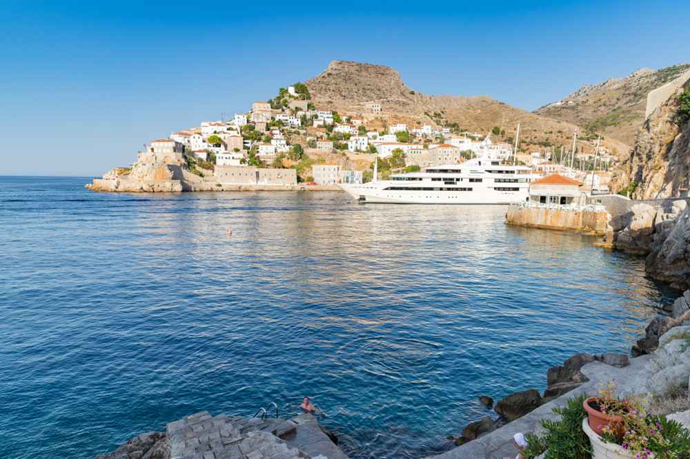 Crystal-clear water in a cove reached on Hydra boat trips, with a boat moored below the stone town