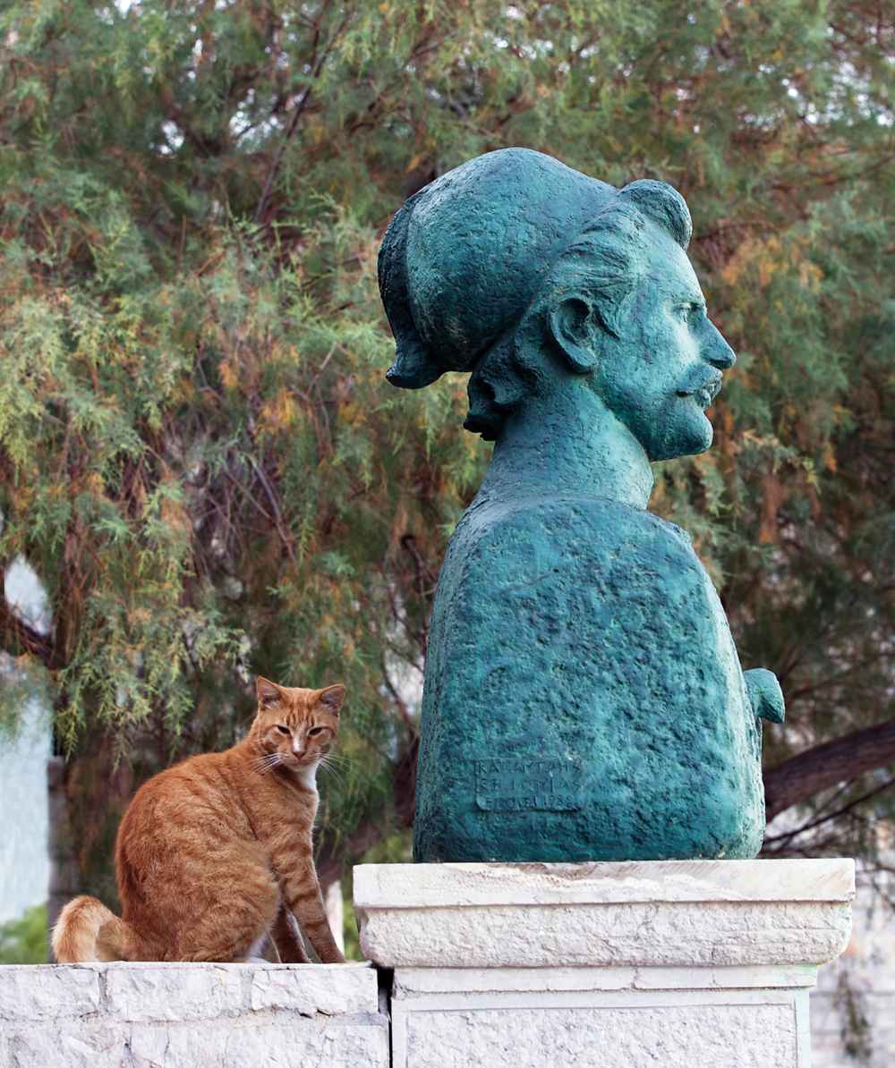A ginger Hydra cat beside a bronze bust in the town