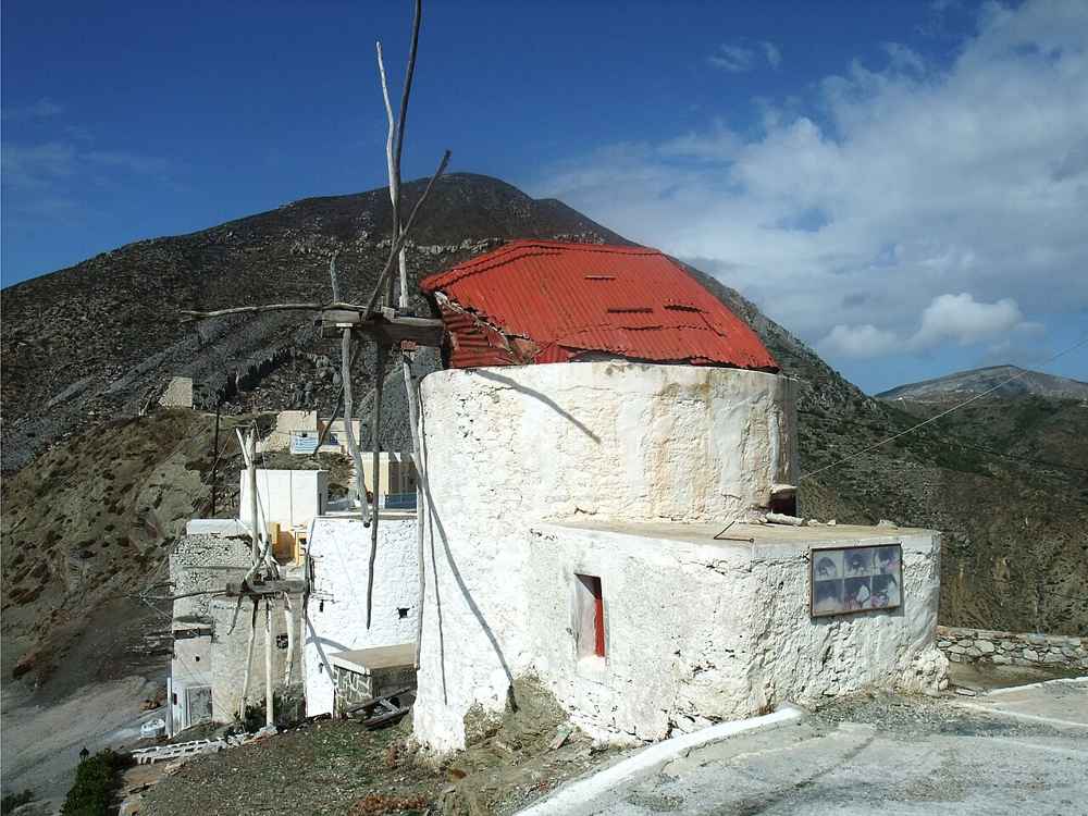 A restored stone windmill with a red roof on the ridge above Olympos, Karpathos