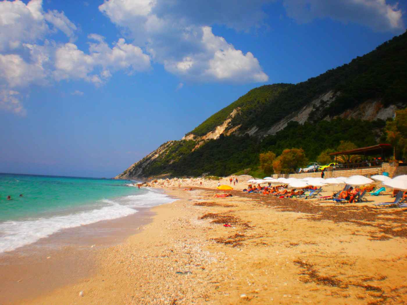 A golden sandy beach below green cliffs on the coast of Lefkada