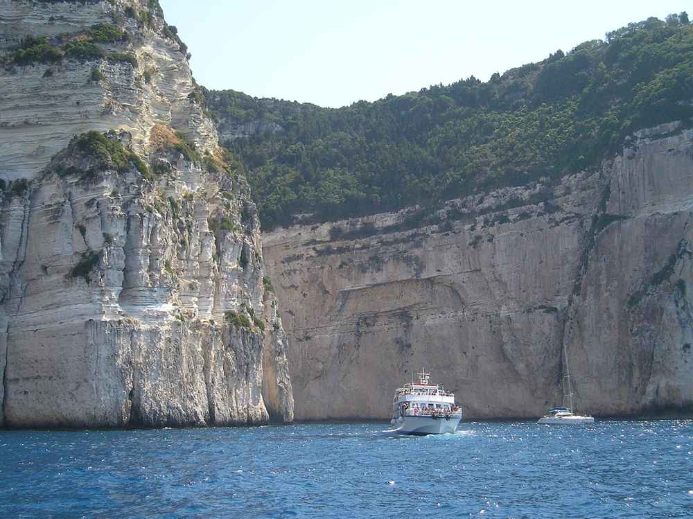Excursion boat beneath the white cliffs and blue caves of the Paxos west coast