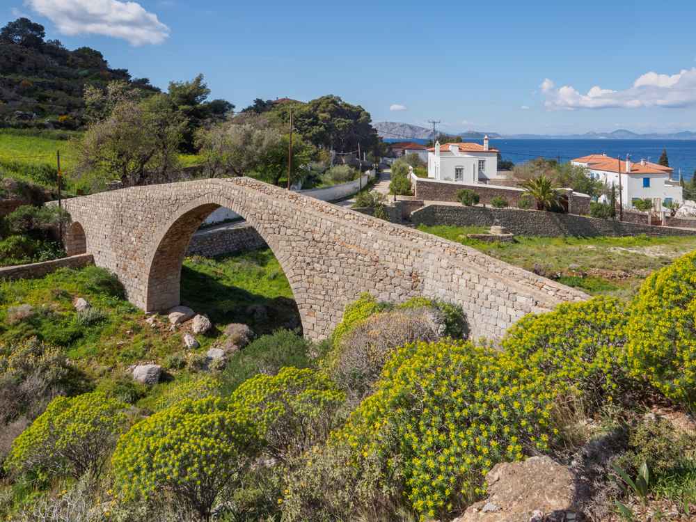 Vlychos Hydra: the old arched stone bridge above the beach, with the sea and Peloponnese beyond