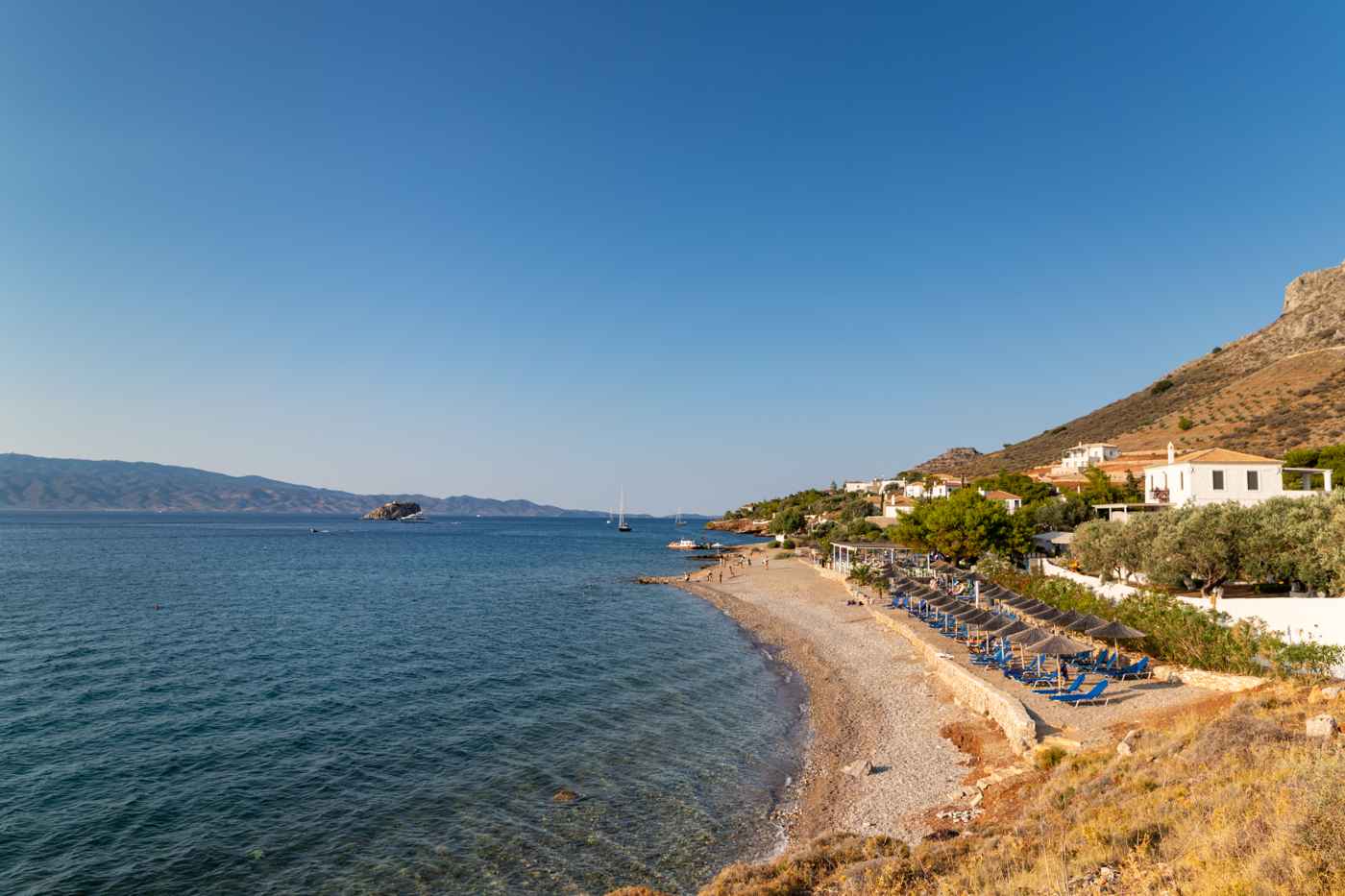 Vlychos and Plakes beach on Hydra, clear water and sunbeds below the hillside