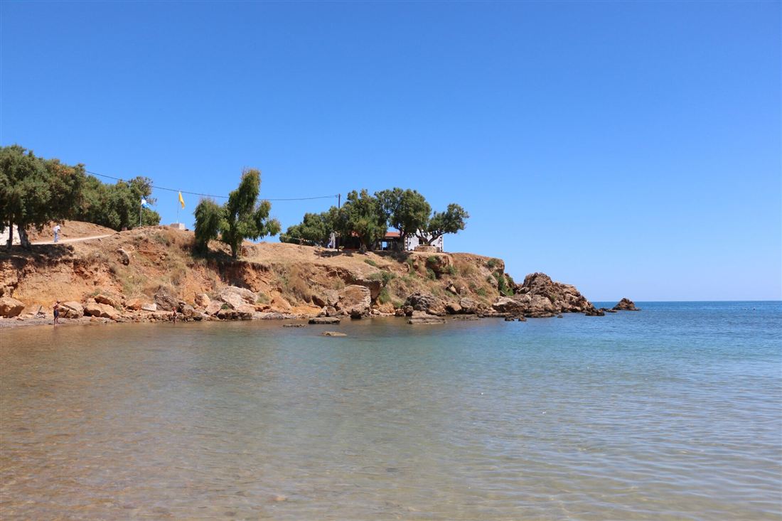 The turquoise sandy cove at Agioi Apostoli near Chania with its pine-topped chapel headland