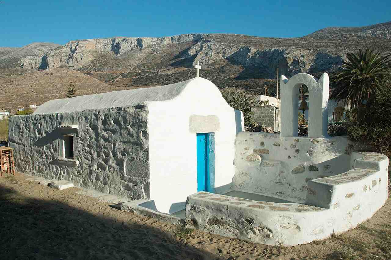 A whitewashed stone chapel on the sandy beach of Aegiali, beneath the mountains of northern Amorgos