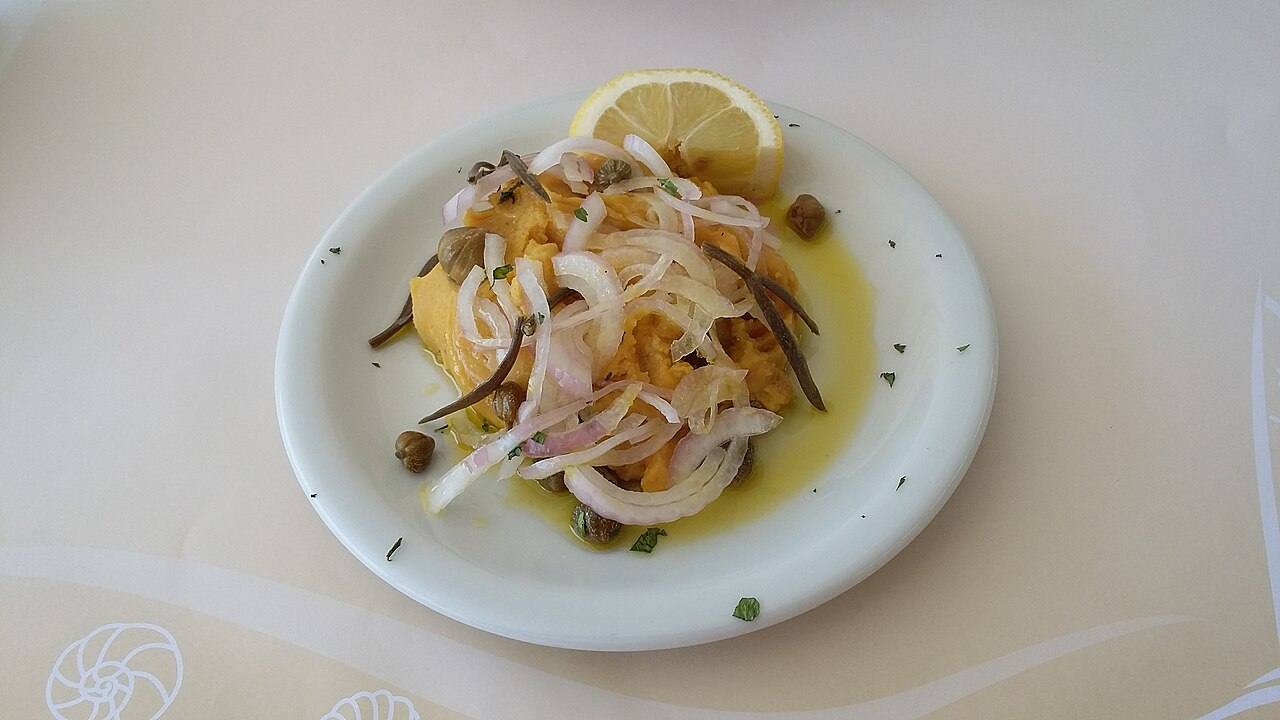 A plate of Cycladic fava topped with raw onion, capers and lemon, a signature dish of the Amorgos table