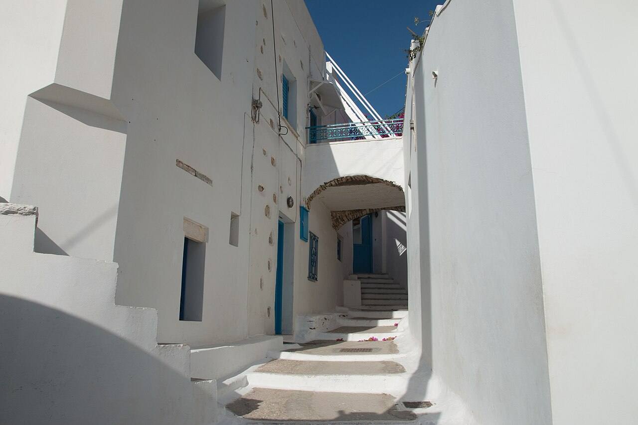 A bright whitewashed alley with an arch and blue doors in the mountain village of Langada, Amorgos