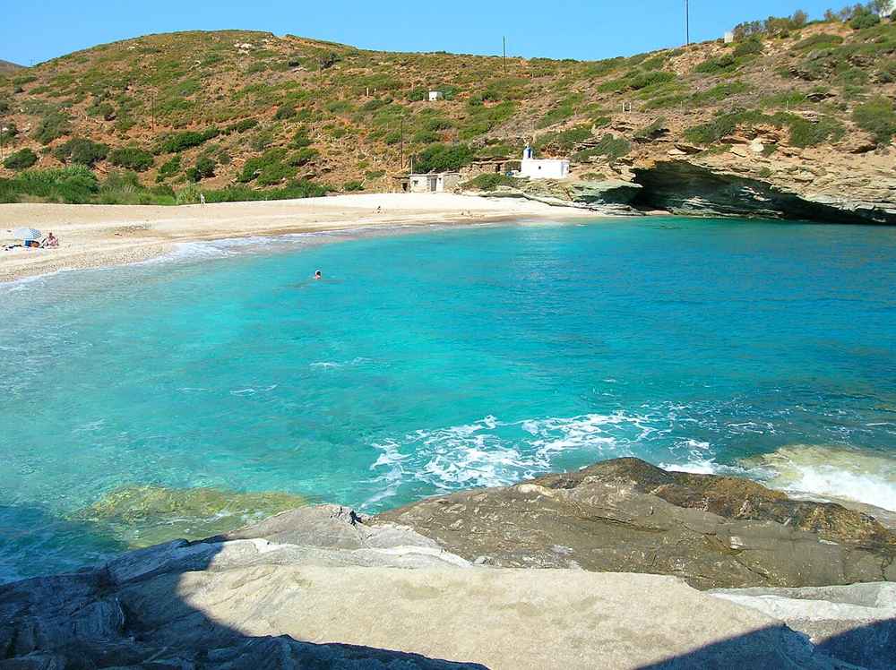 A turquoise cove with golden sand and a small chapel on the coast of Andros