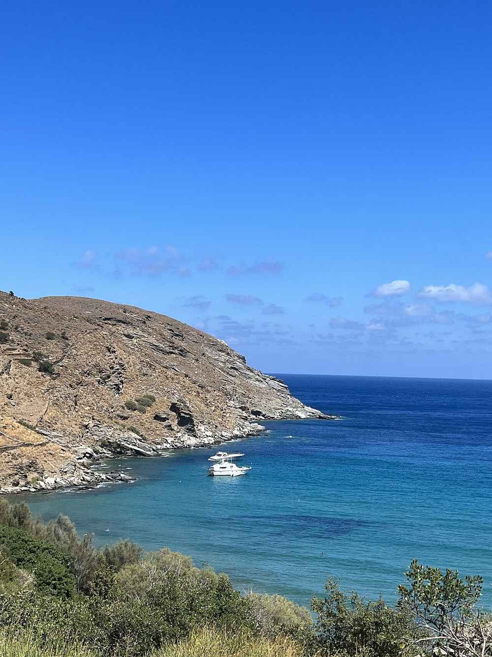 A boat anchored in a secluded turquoise cove on the rugged coast of Andros