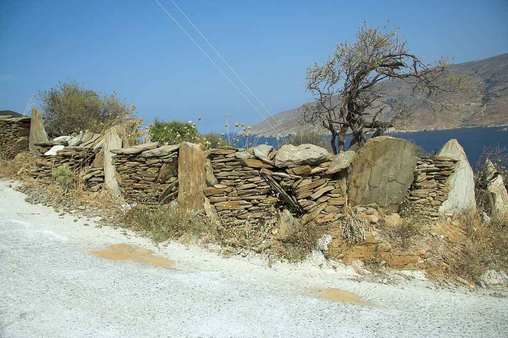A quiet island road running past a dry-stone wall with a view over the sea on Andros