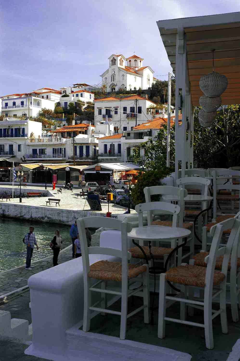 A whitewashed seafront taverna terrace at Batsi on Andros, the village and church rising behind