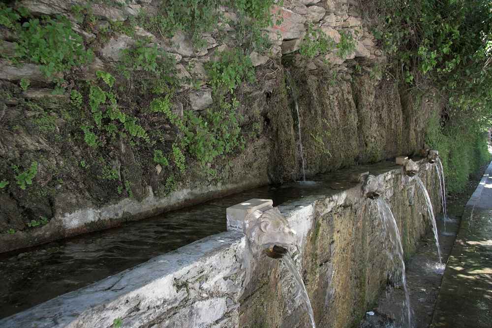 Spring water flowing from carved marble lion heads at Menites in the green interior of Andros