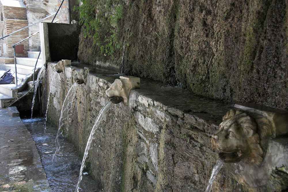 Spring water pouring from carved marble lion heads at the village of Menites on Andros