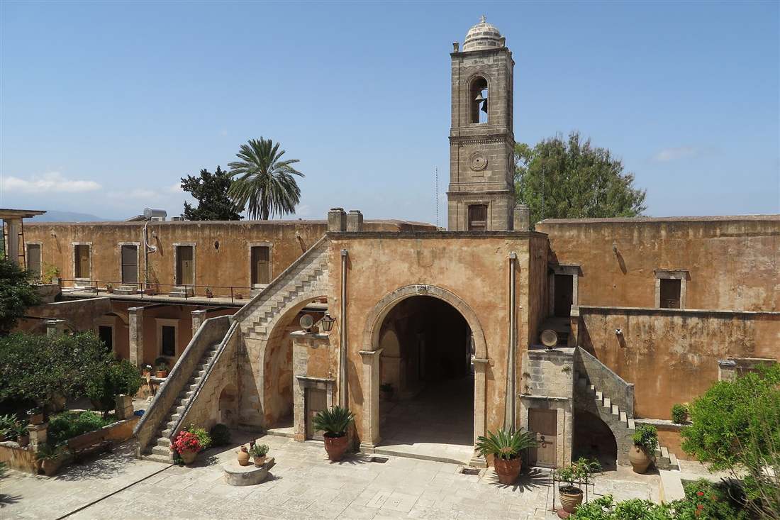 The courtyard, ochre church and bell tower of the Venetian-era Agia Triada Tzagarolon Monastery on Akrotiri, Crete