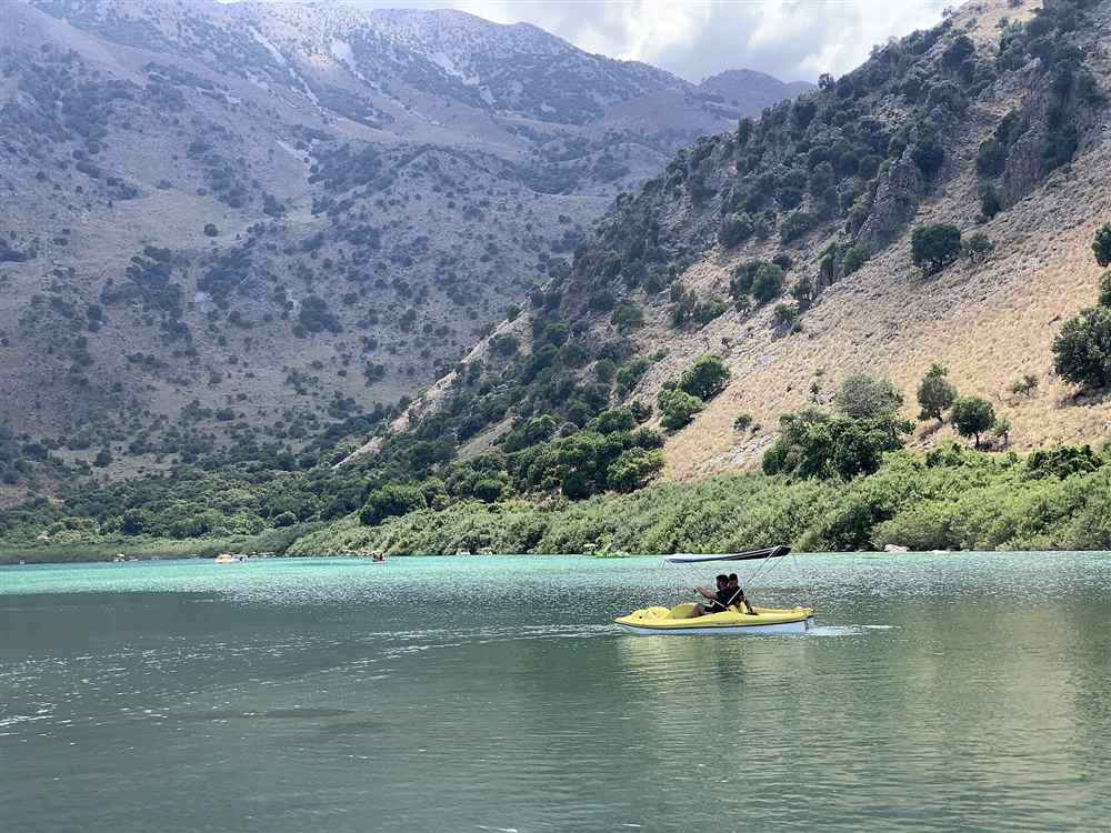 A yellow pedal boat on the green water of Lake Kournas below the Apokoronas hills in Crete