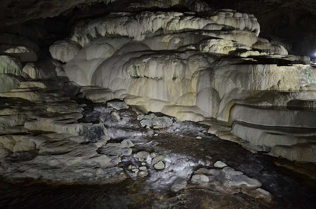 The illuminated flowstone formations and thermal stream inside Kaklik Cave