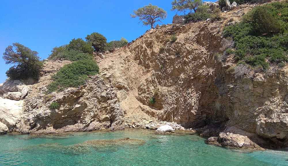 A clear turquoise cove below the green hills of central Karpathos in summer