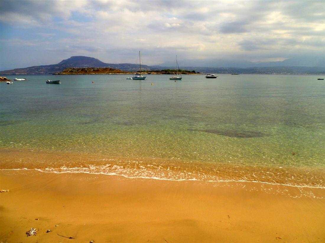 Marathi beach, Akrotiri, Crete: the sheltered sandy cove and turquoise Souda Bay water with the offshore islet and moored boats