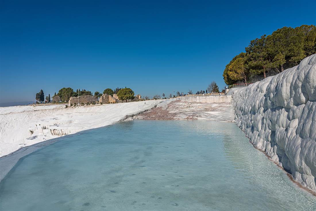 A turquoise thermal pool against the white travertine wall of Pamukkale