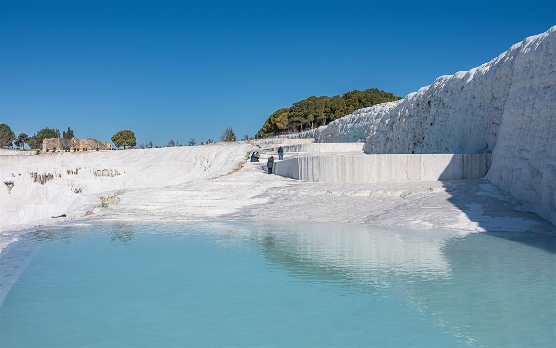 The white travertine terraces and thermal pool of Pamukkale under a clear sky
