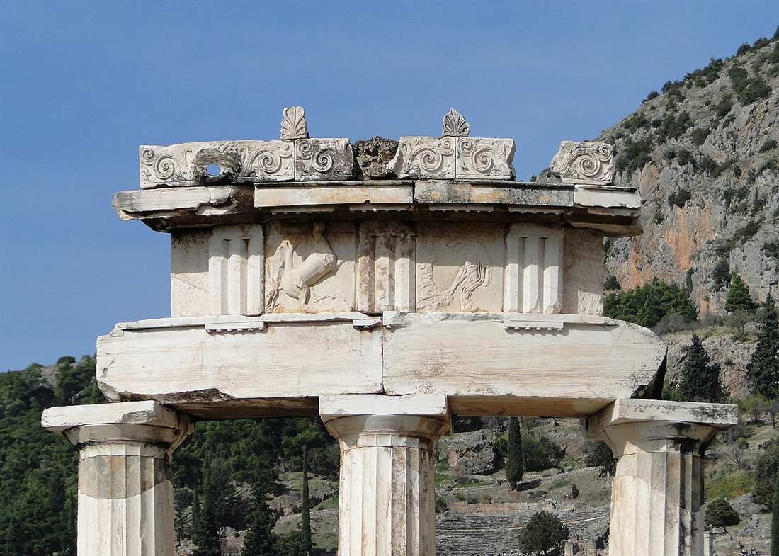 The carved frieze and Ionic-scroll cornice of the Tholos of Delphi against the slopes of Mount Parnassus