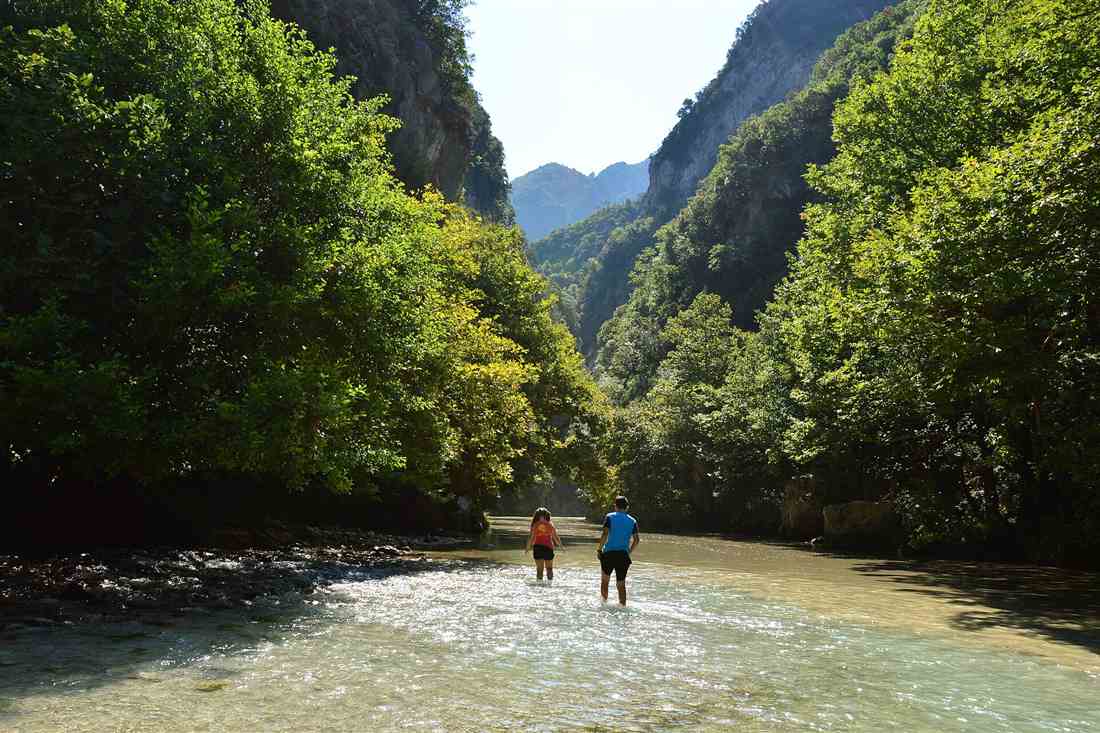 Walkers wading up the clear shallow Acheron between the gorge walls at Glyki, the water the kayak runs launch into