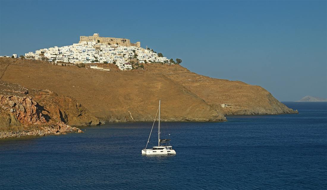 A catamaran anchored below the Chora and Querini castle of Astypalaia on an Astypalaia yacht charter