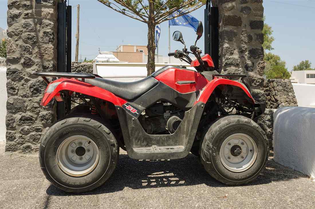 Athens ATV tour quad bike: a red ATV parked at a volcanic-stone gate under the Greek flag