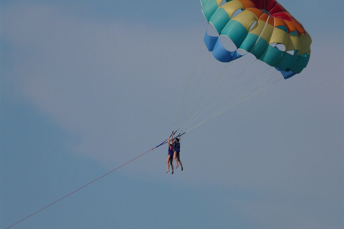 Corfu parasailing: two flyers under a rainbow parasail canopy on the tow line above the Corfu coast