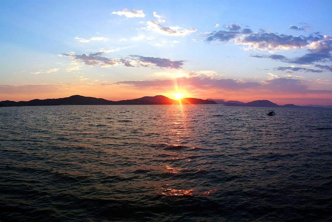 The sun going down over the sea off Corfu with a boat at anchor