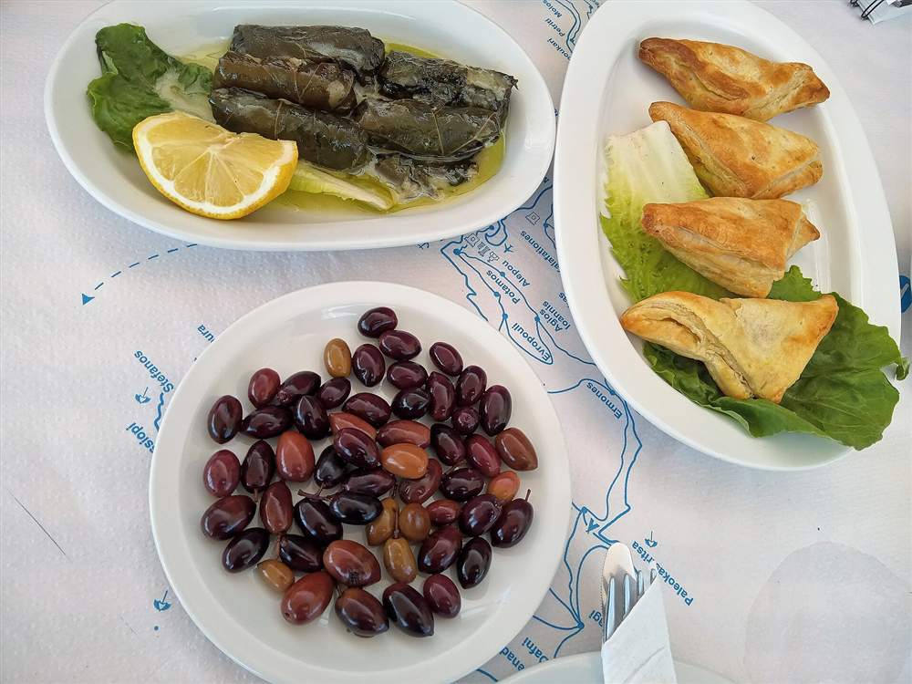 A Cretan taverna table with dolmades, olives and freshly baked cheese pies