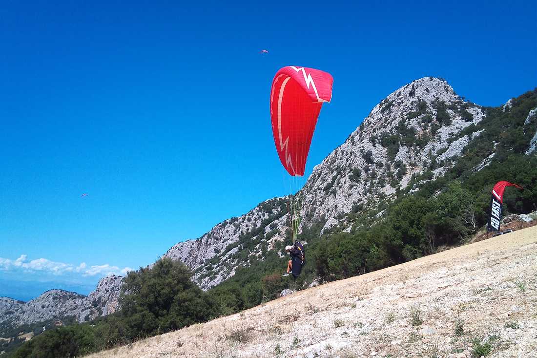 Crete paragliding: a red paraglider wing lifting off a mountain take-off slope above the sea in Greece