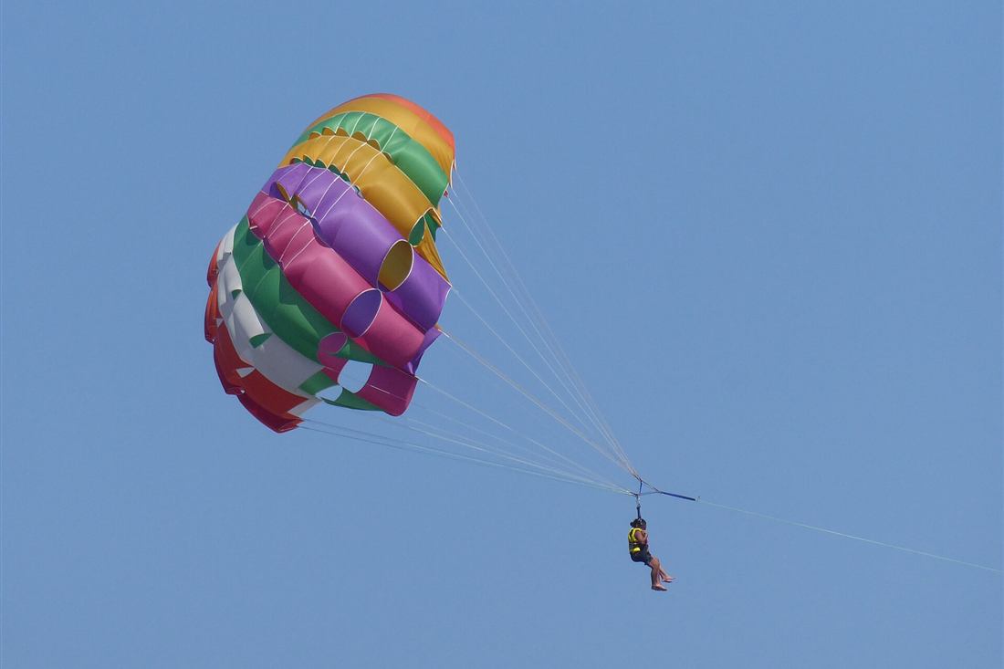 Crete parasailing: a rainbow parasail canopy carrying a flyer high above the sea at Agia Marina, Crete