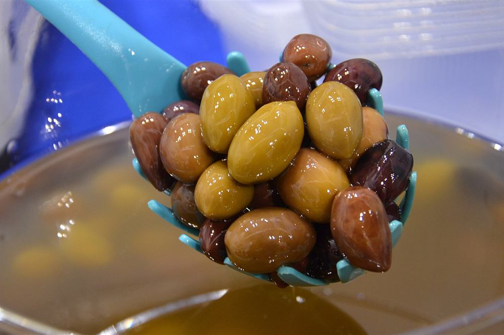 Glossy green and purple olives lifted on a slotted spoon at a market stall, the cured fruit of the Kavala plain