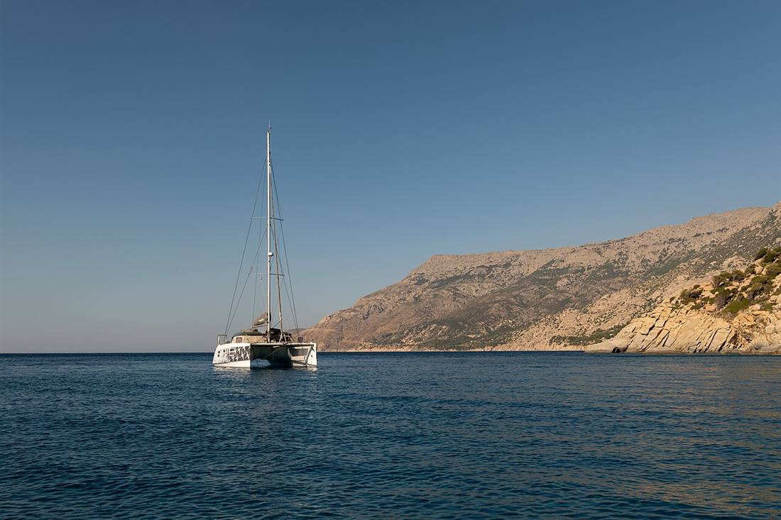 A sailing catamaran at anchor in clear water off a Greek island coast