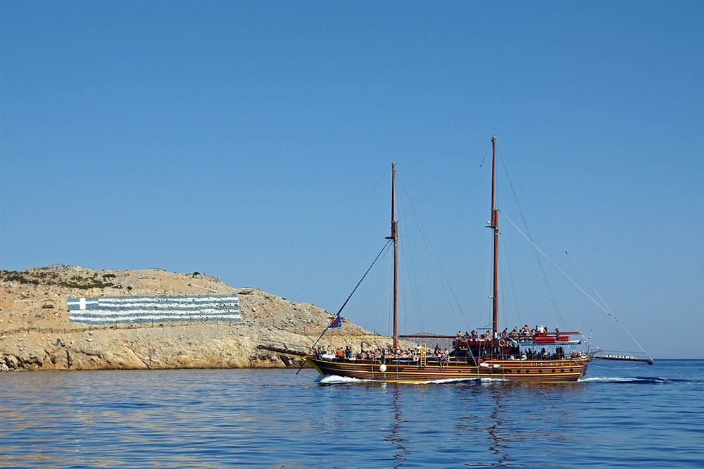 Wooden caique cruising past a rocky headland off Kos