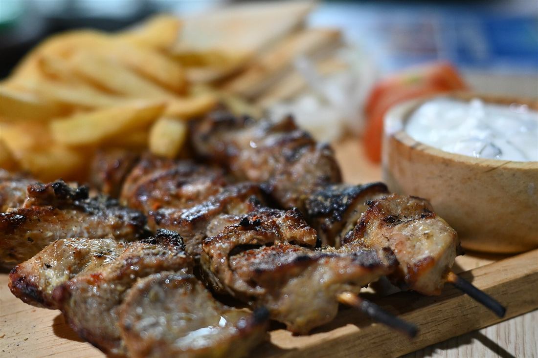 Grilled pork souvlaki skewers with chips and tzatziki on a wooden board, the street-grill stop on a Mykonos food tour