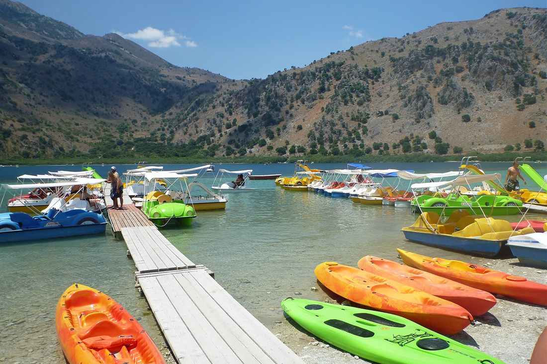 Mykonos kayak tour: bright sit-on-top kayaks lined up on a wooden jetty over clear water in Greece
