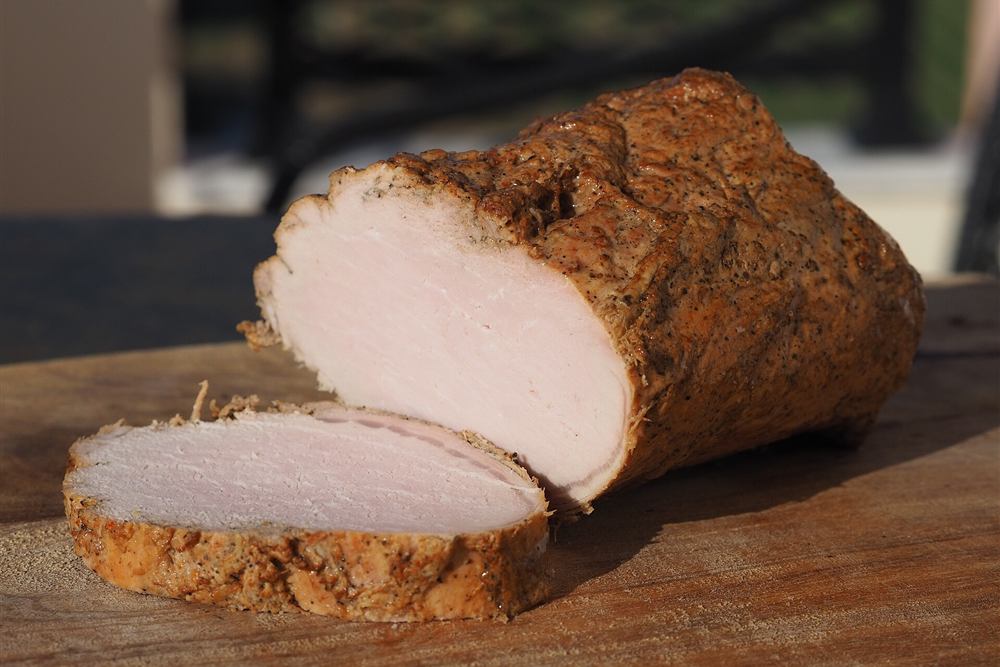 A cured and smoked pork loin sliced on a wooden board, the charcuterie tasted at a village grocery