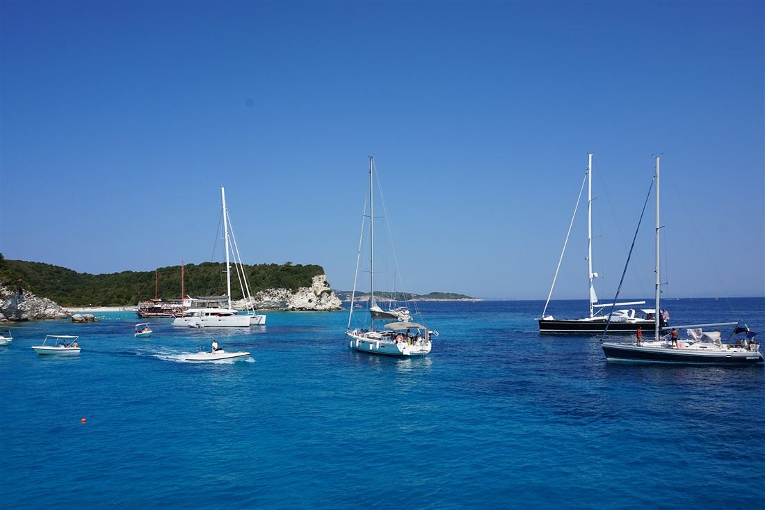 Boats anchored in the turquoise water off Antipaxos with a day-cruise vessel at the beach, the swim stop on a Parga to Paxos boat trip