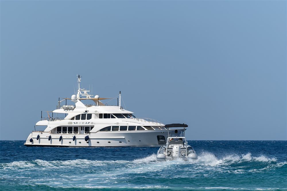 A self-drive rigid inflatable running past an anchored yacht on Cycladic water
