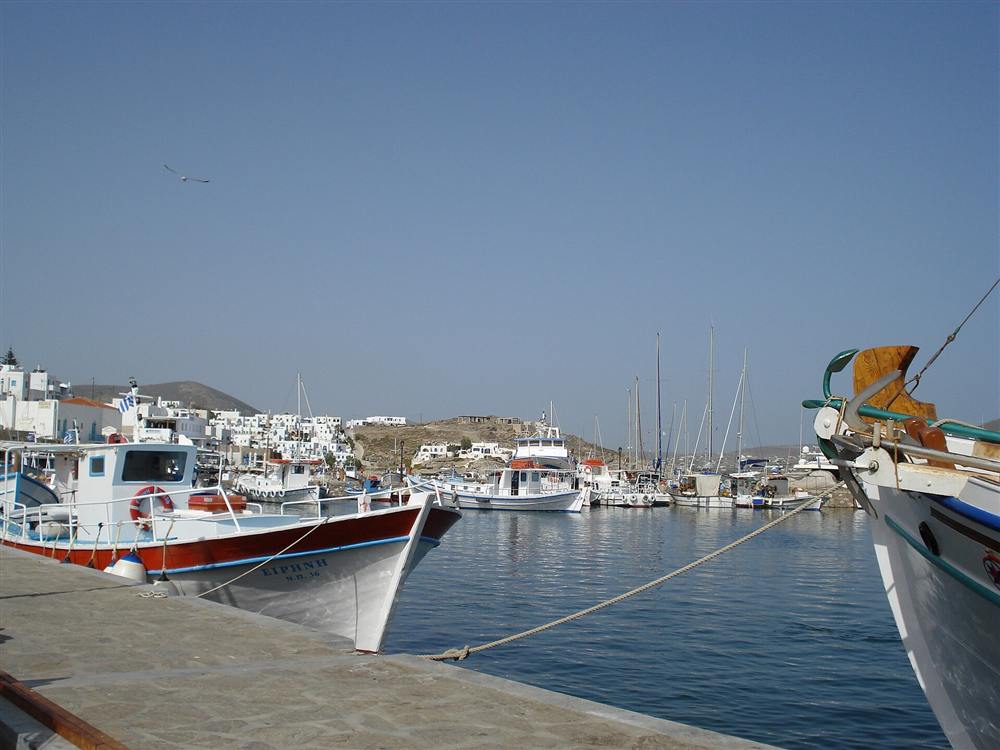 Painted wooden fishing boats moored along the quay in Naoussa harbour below the white village