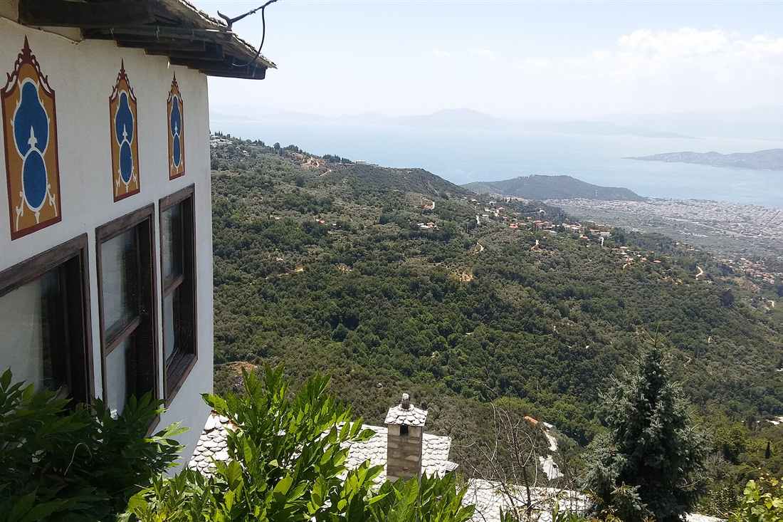 A painted Pelion mansion above the slate roofs of Makrinitsa with Volos and the Pagasetic Gulf below, the balcony view on a Pelion villages tour