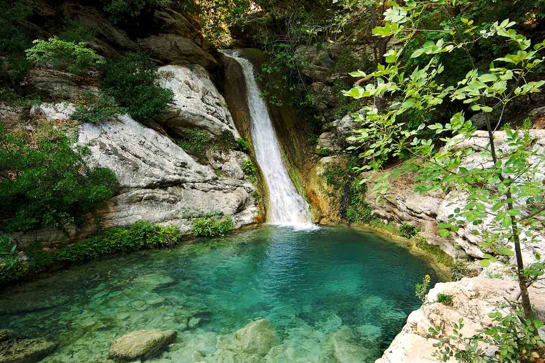 A waterfall dropping into the clear emerald plunge pool of the Polylimnio waterfalls in the Messinian gorge